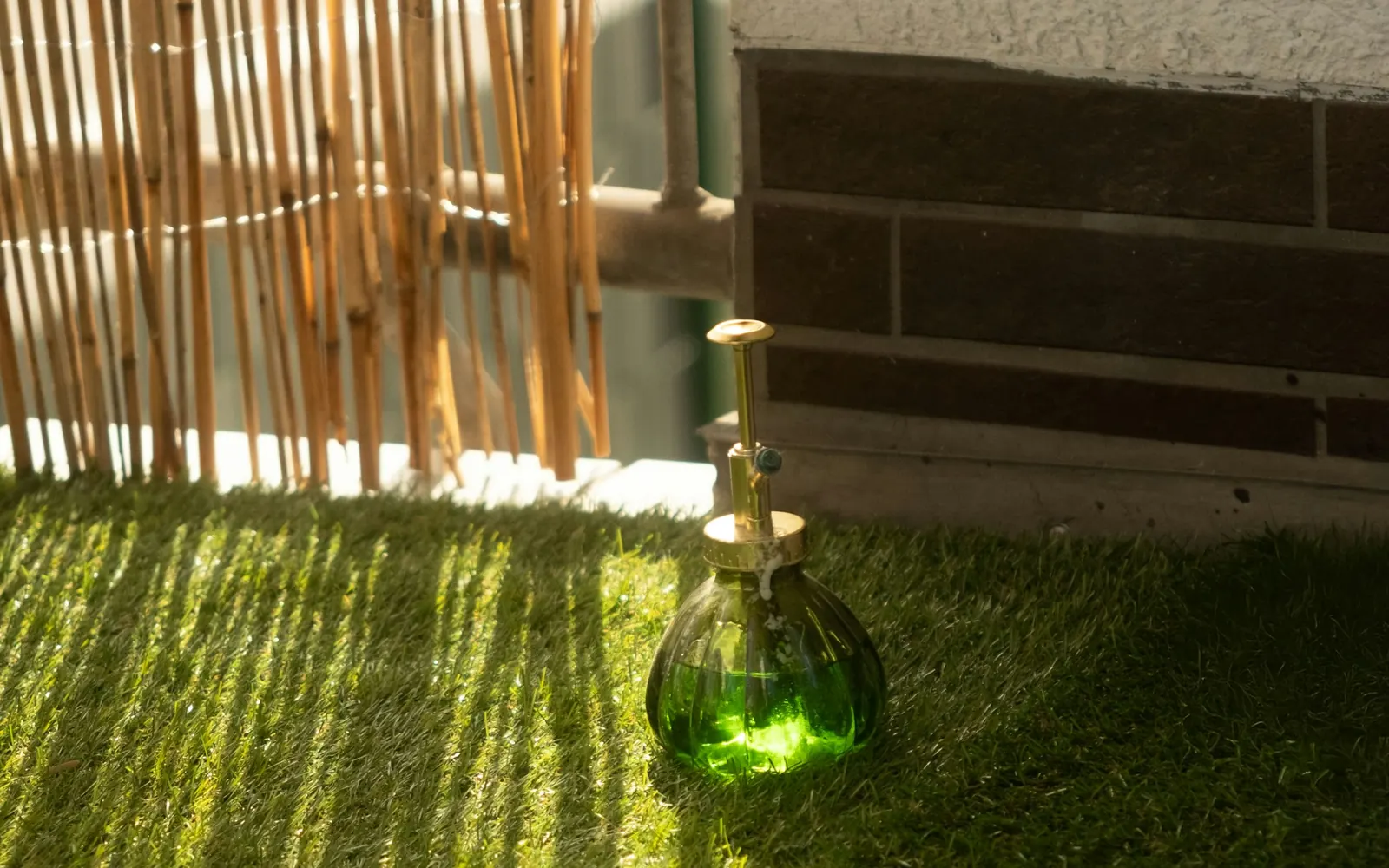 Artificial grass laid up to the wall of an apartment balcony, with a bamboo screen on the railing casting striped shade across it