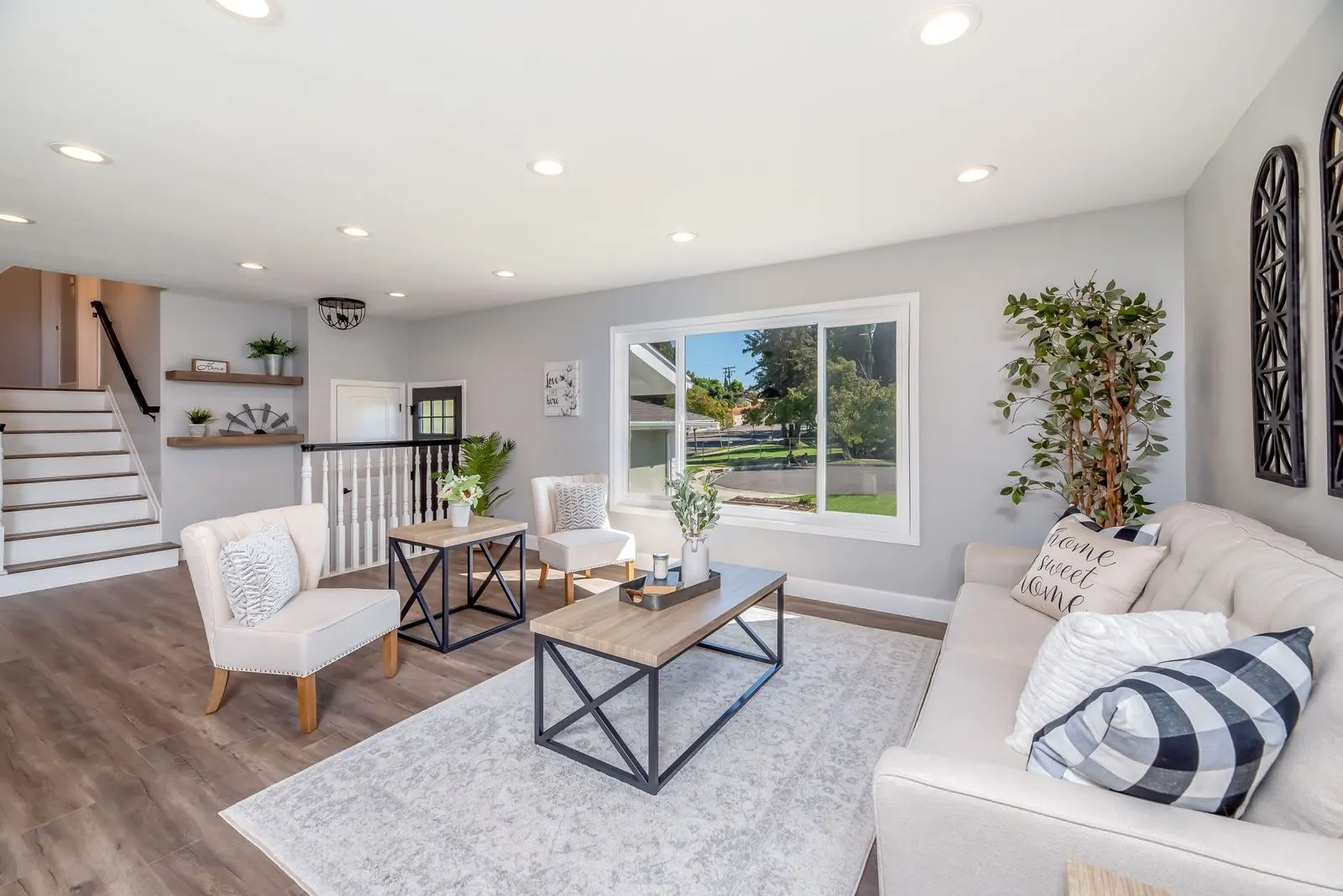 Living room with a grey wood-look plank floor, a large pale grey rug under the coffee table, a cream tufted sofa and two armchairs, with a band of floor showing around the rug