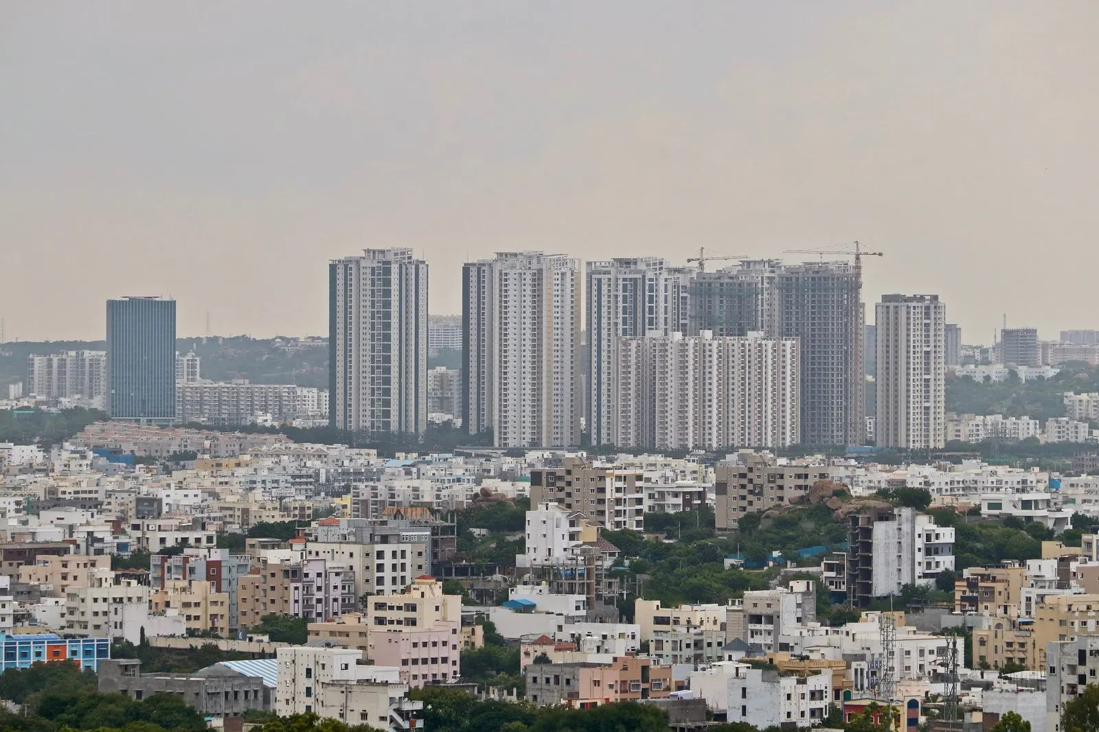 View from Golconda hill over dense low-rise houses and apartment blocks, with a row of new high-rise towers and cranes in Madhapur behind them