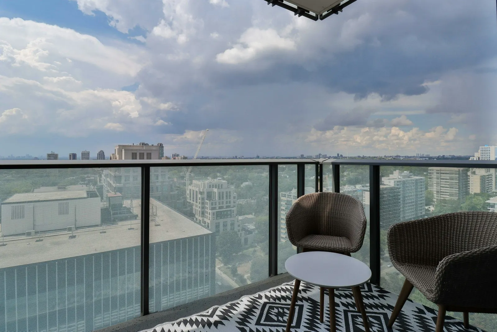 High-rise apartment balcony with a glass railing, two wicker chairs and an open city view
