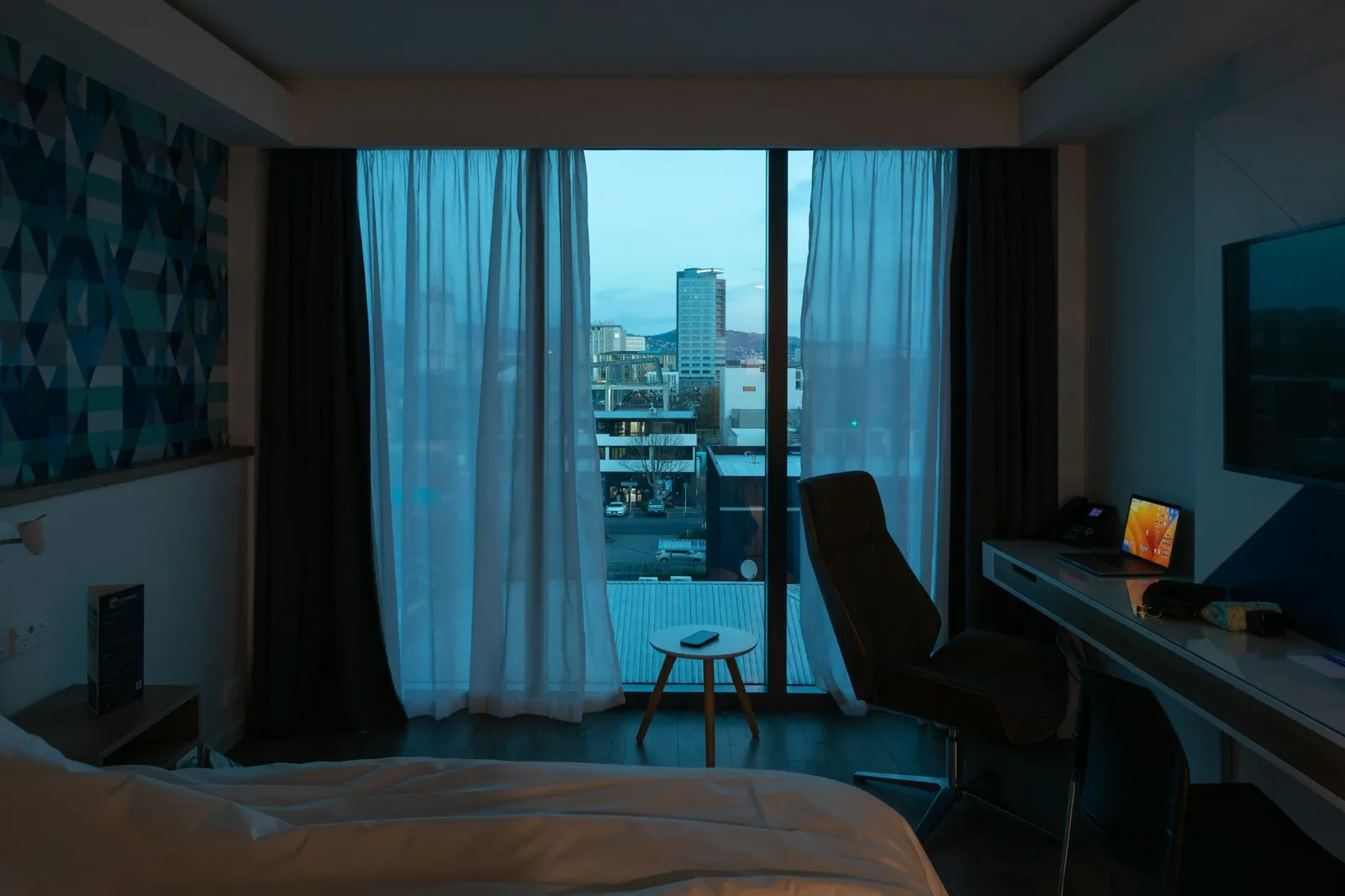 Floor-to-ceiling window with layered sheer and dark blackout curtains, half open to a city view