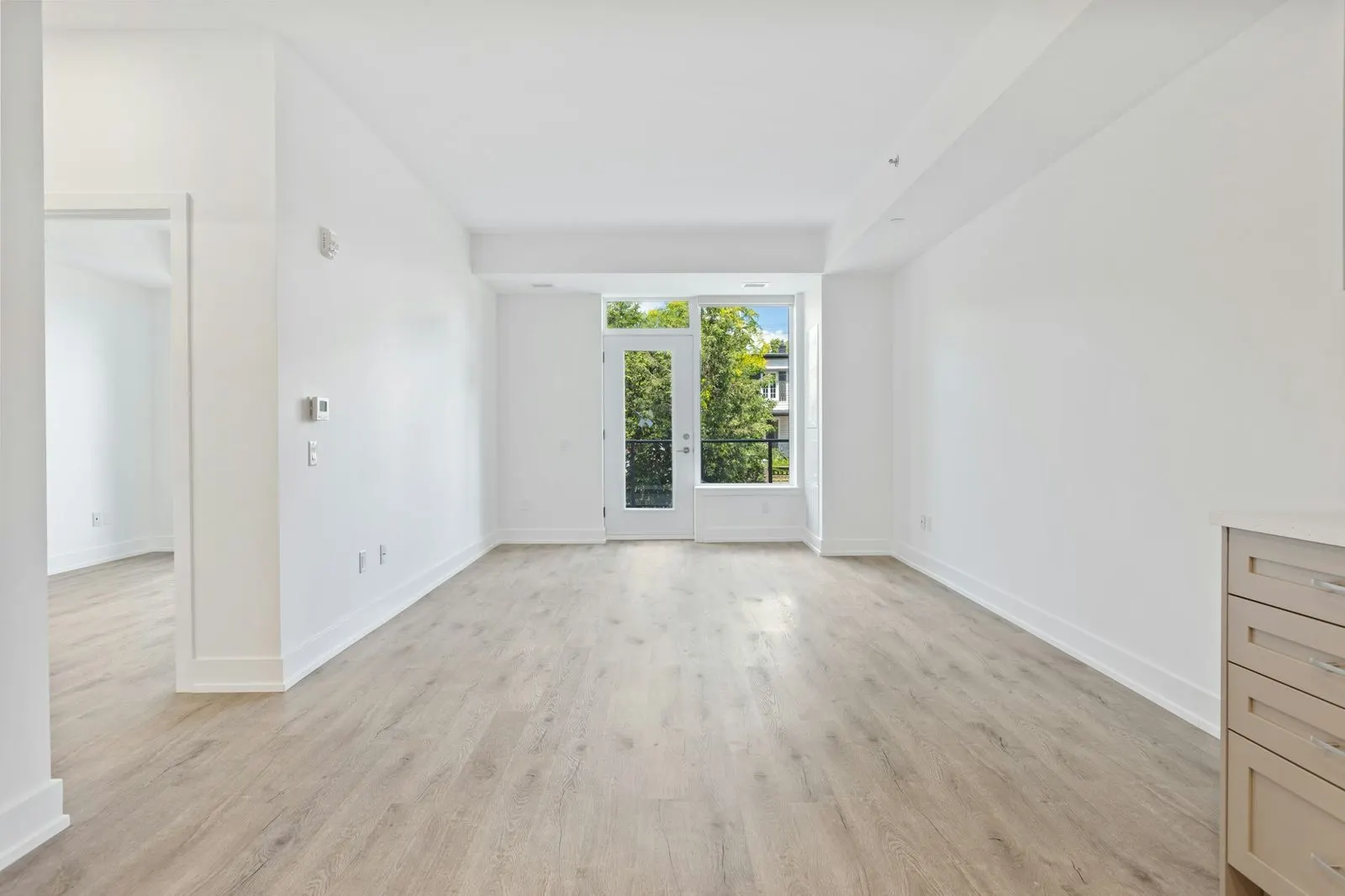 Empty new apartment with bare walls, wood-look flooring and a glass balcony door at the far end