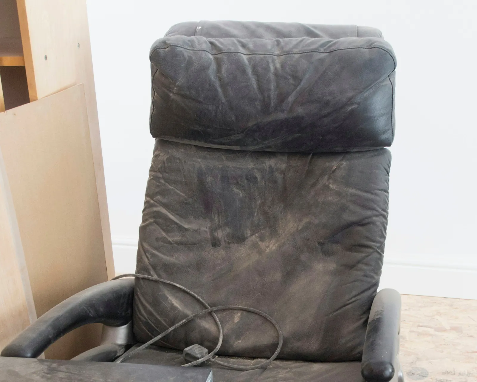 Worn black leather recliner with creased, scuffed upholstery, due for repair