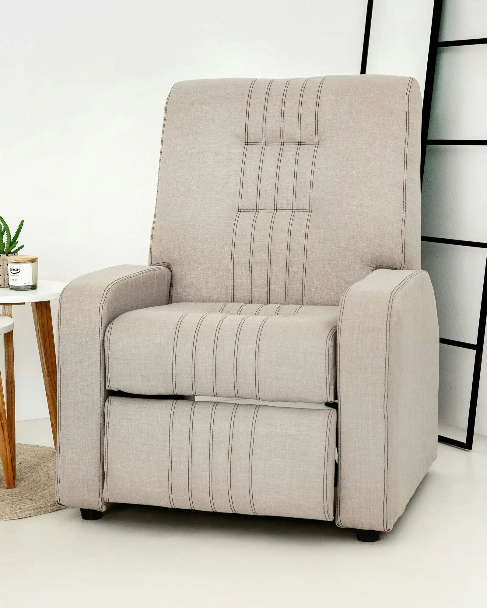 Beige fabric recliner armchair with channel stitching running down the back, across the seat front and onto the folded footrest panel