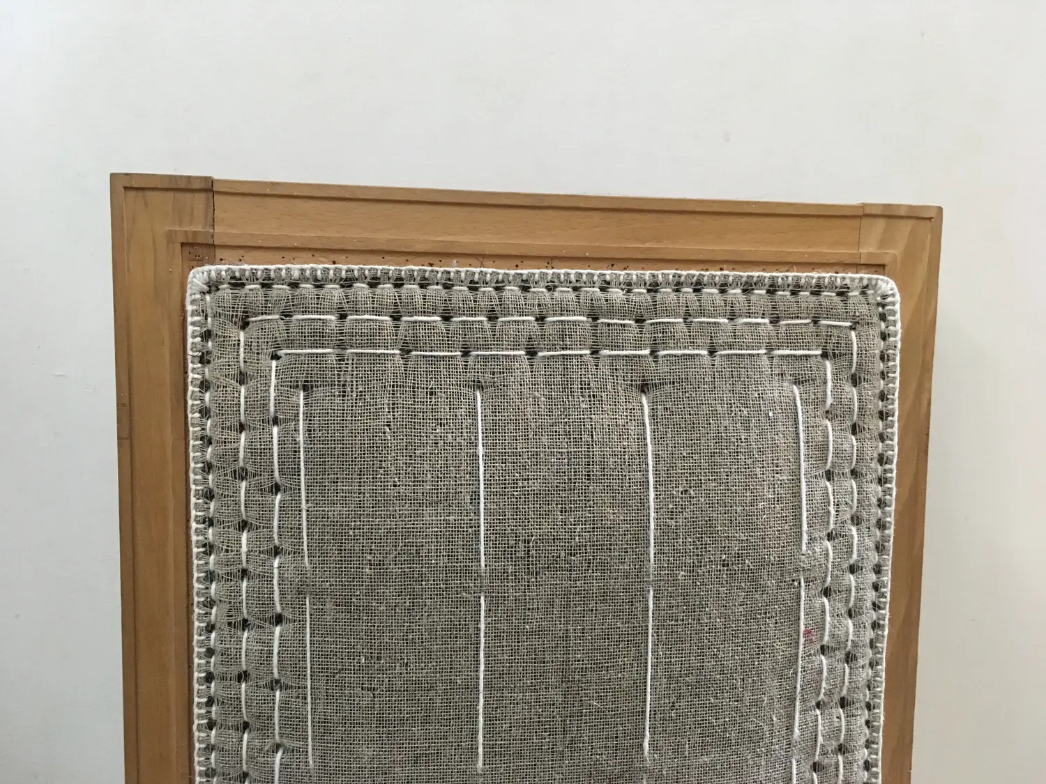 Chair back being reupholstered on its wooden frame: hessian over the stuffing, shaped with hand-stitched edge rolls and rows of stitching before the top fabric goes on