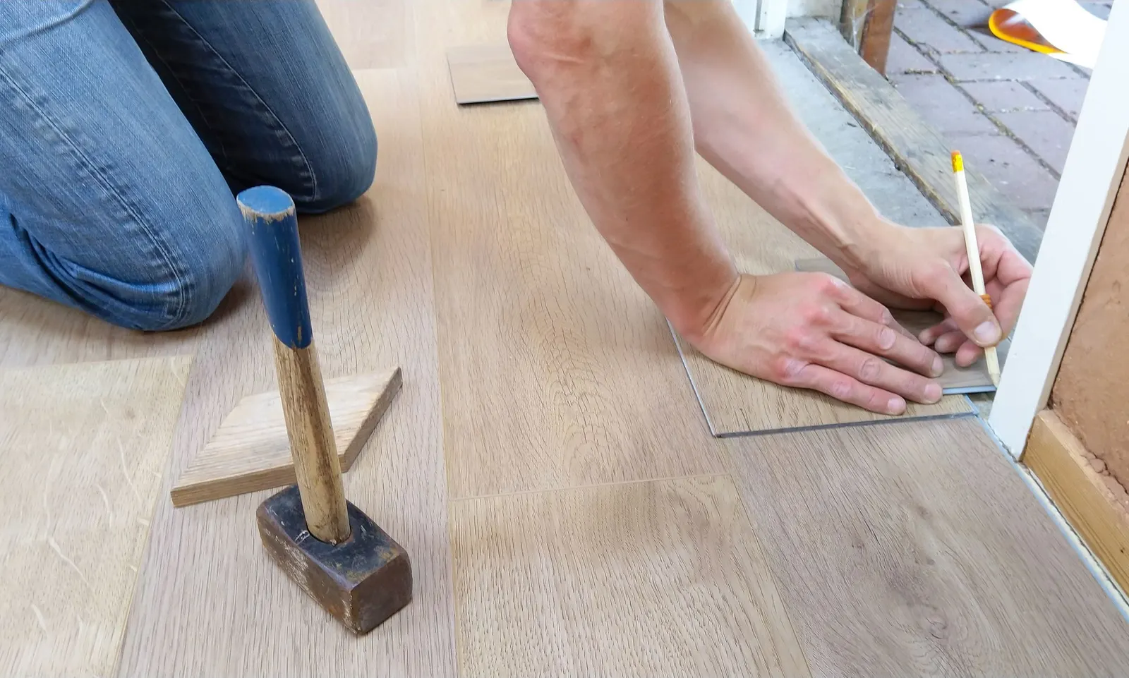 Installer marking a light oak-look click plank with a pencil, a mallet on the floor beside him
