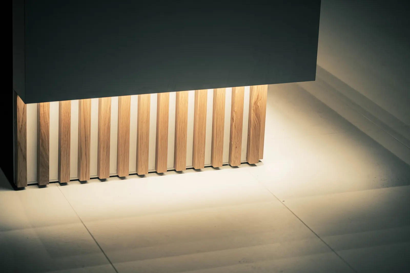 Vertical wooden slat panelling lit from above by a concealed LED strip, with light falling down the grooves