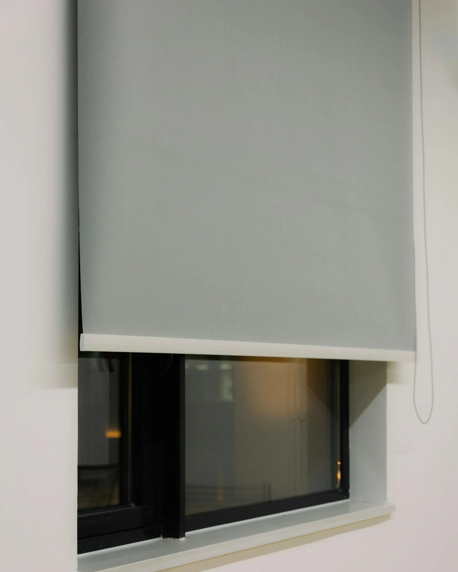 Grey roller blind mounted outside a recessed window and lowered halfway, with its bead chain hanging on the right