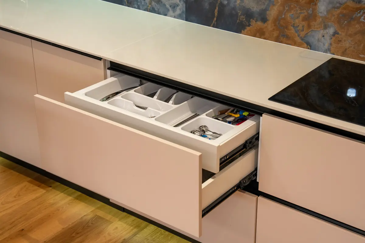 Open inner drawer with a white cutlery organiser below an induction hob in a handle-less kitchen