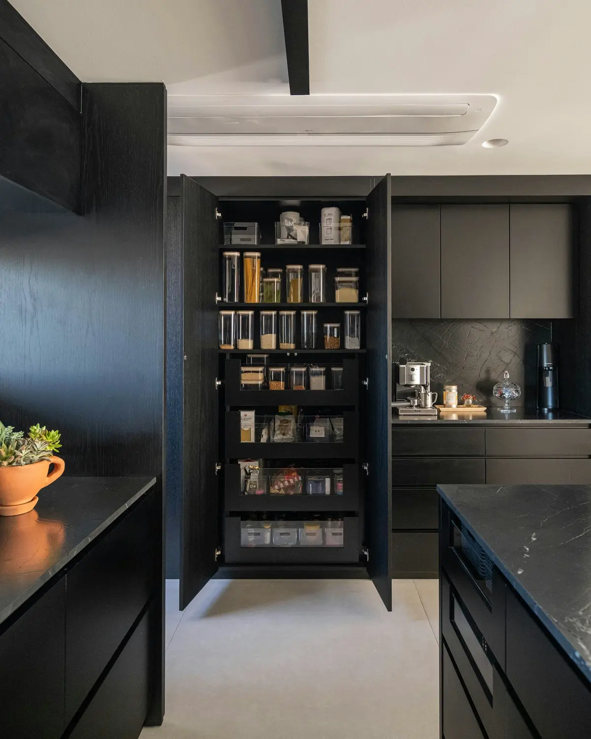Tall black pantry unit with its doors open, showing shelves of storage jars above internal pull-out drawers