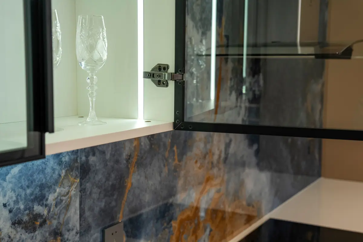 Wall cabinets with clear glass doors in slim black aluminium frames, lit inside, with a concealed hinge on an open door