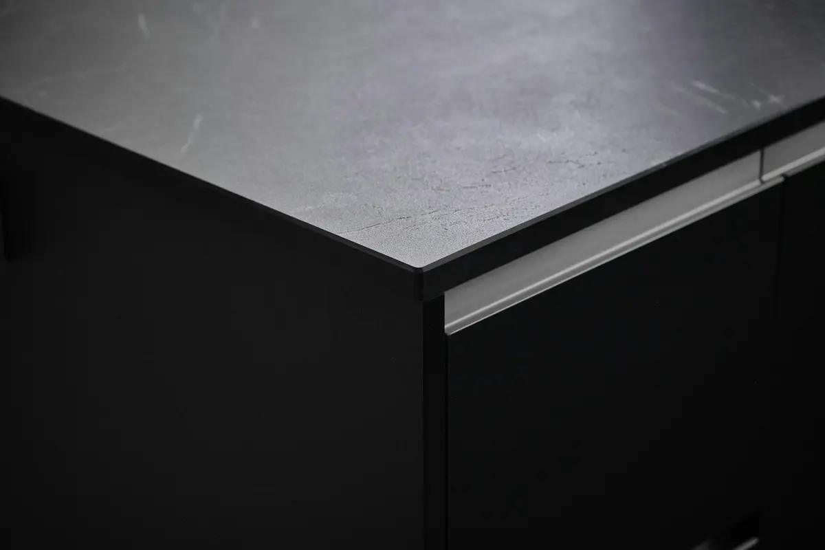 Close-up of a black handle-less base unit with a recessed aluminium grip profile under a thin stone-look counter edge