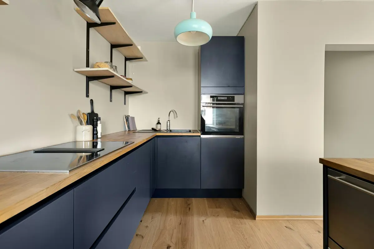 Kitchen with matte navy blue flat shutters, a wooden counter, an induction hob and a built-in oven in a tall unit