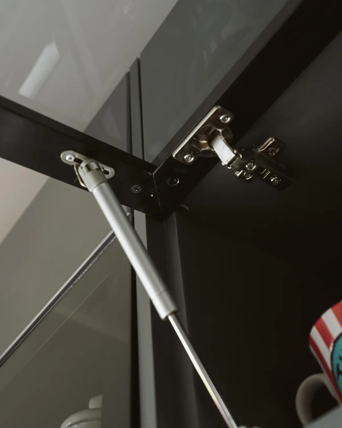 Close-up of a concealed cabinet hinge and a gas strut holding a lift-up wall cabinet door open