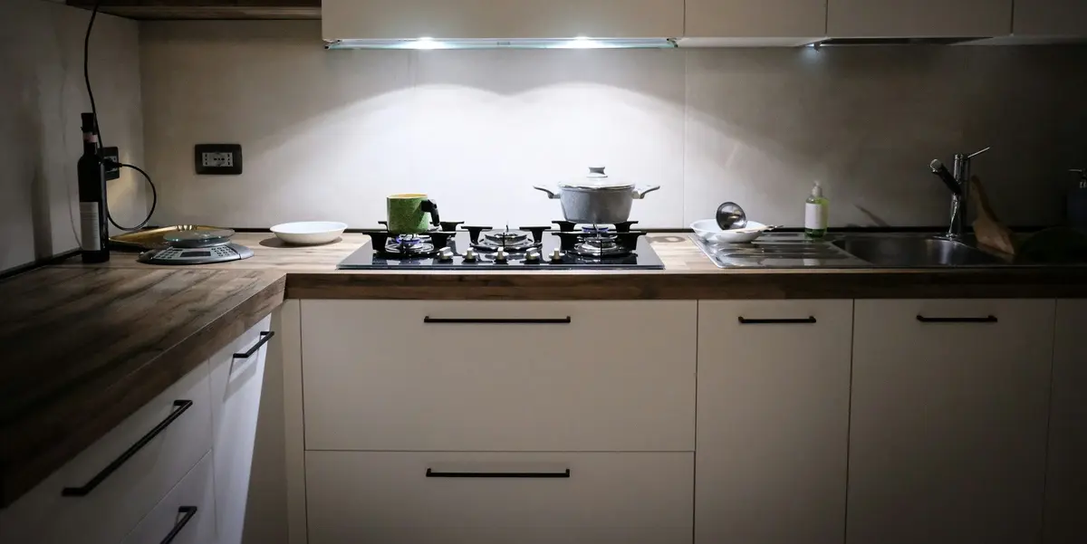 Lights fitted under the wall cabinets shining onto a gas hob and a wooden counter