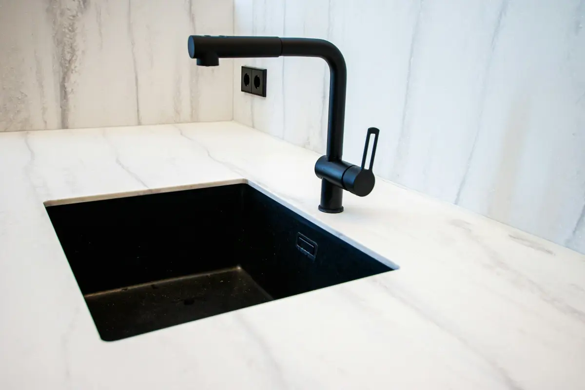 Black undermount sink set into a white marble-look counter with a black pull-out mixer tap