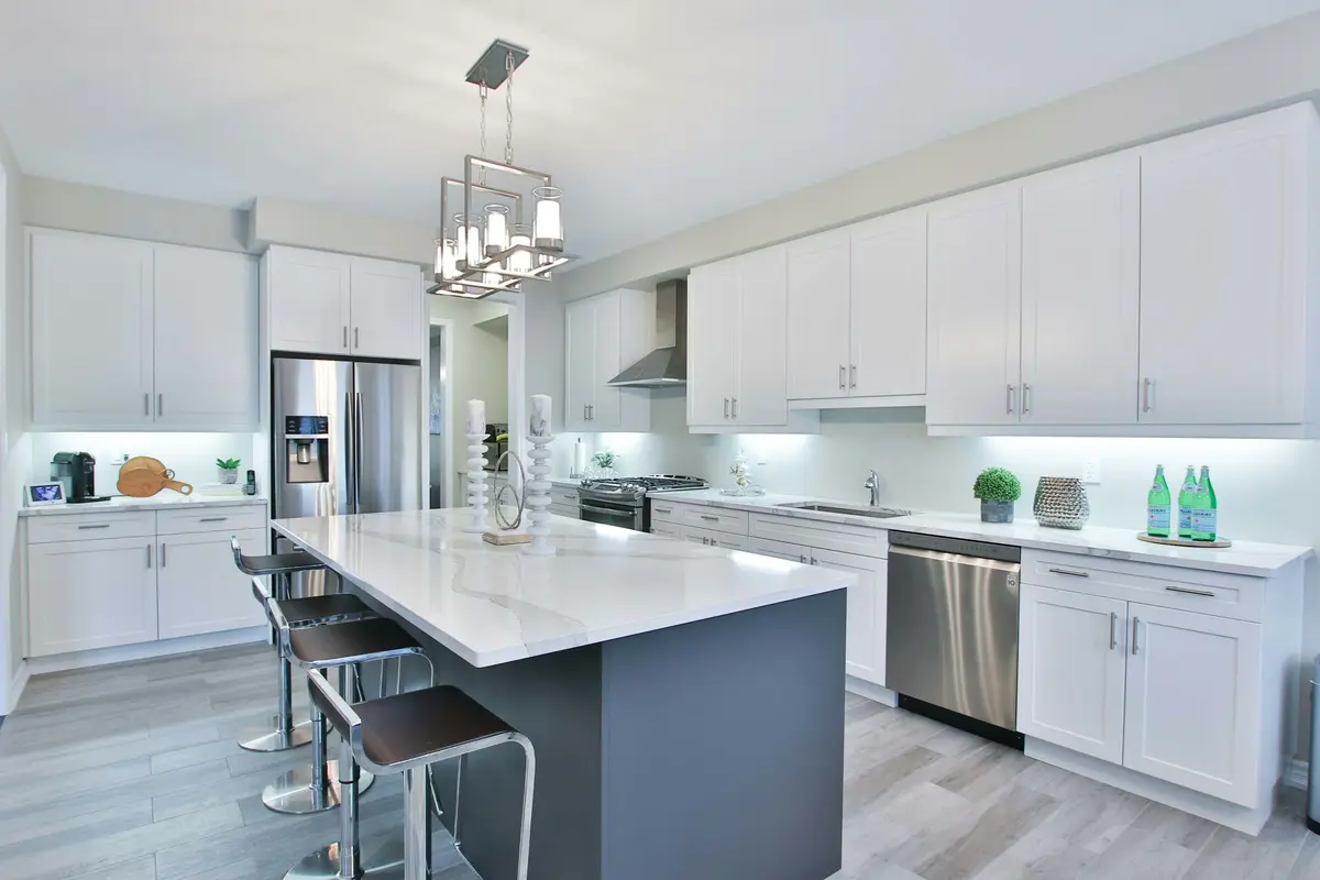 Kitchen with white cabinets along two walls and a separate island with a white marble-look top, a dark grey base and bar stools