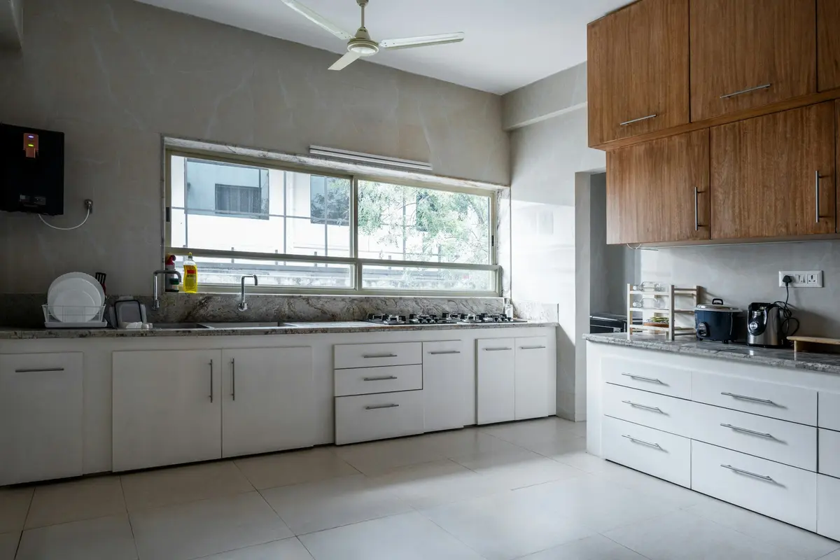 L-shaped kitchen with white base units and drawers, a granite counter, a gas hob and sink under a wide window, and wood-finish wall cabinets on the return wall