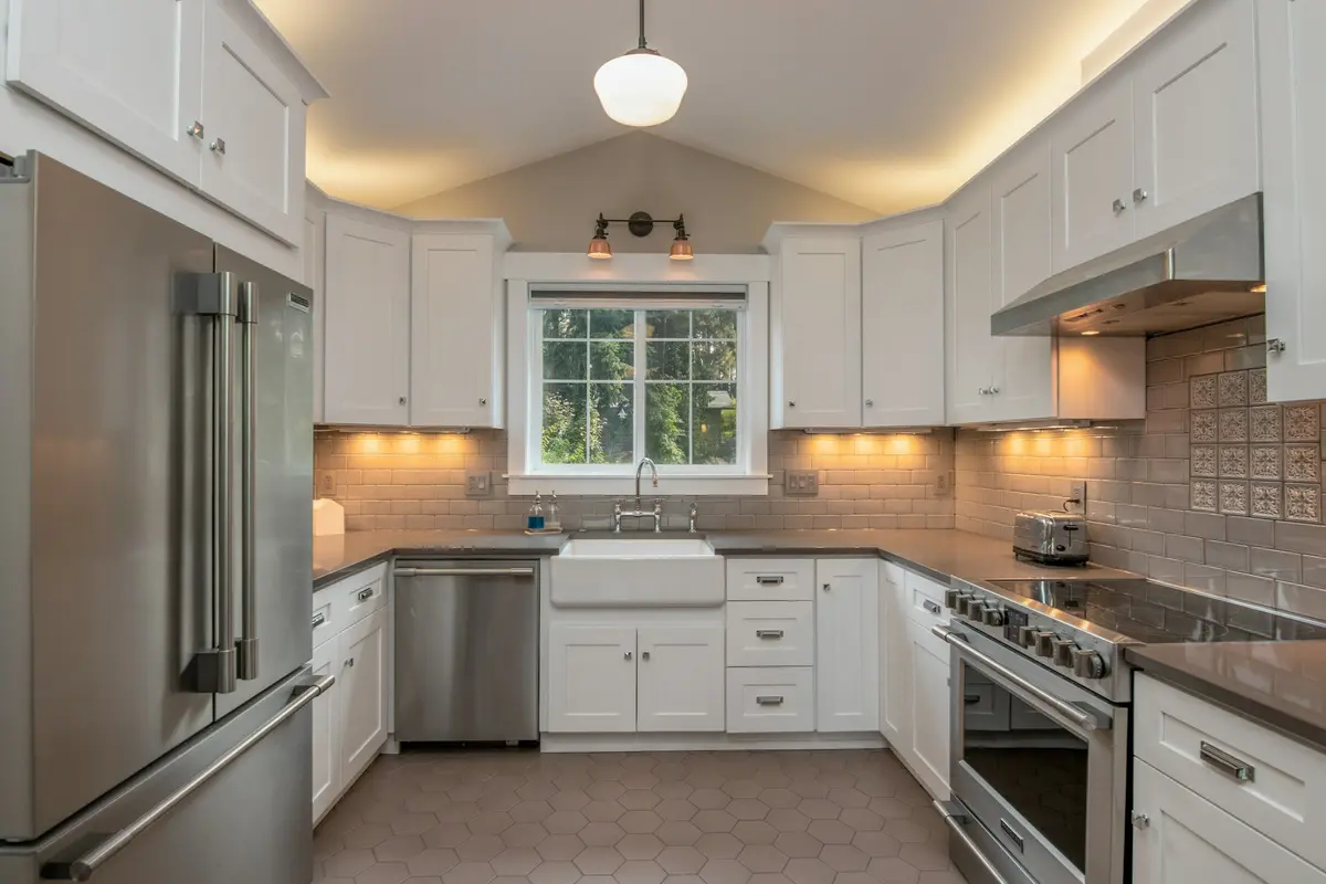U-shaped kitchen with white shaker cabinets on three walls, a sink under the window, a range with a hood and lights under the wall cabinets