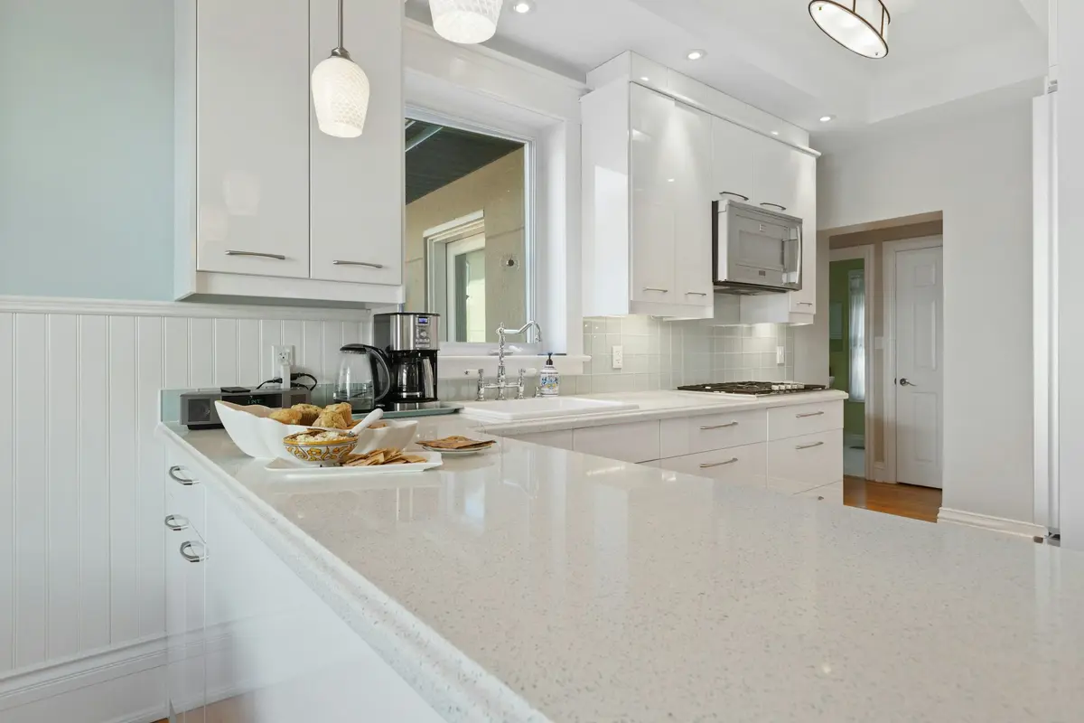 White speckled quartz-look counter running along an L-shaped kitchen with white gloss cabinets