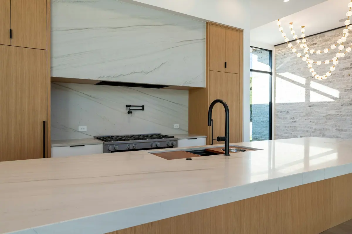 Large-format marble-look slabs on a kitchen island top, the backsplash and the hood surround, with oak cabinets and a black pull-down tap
