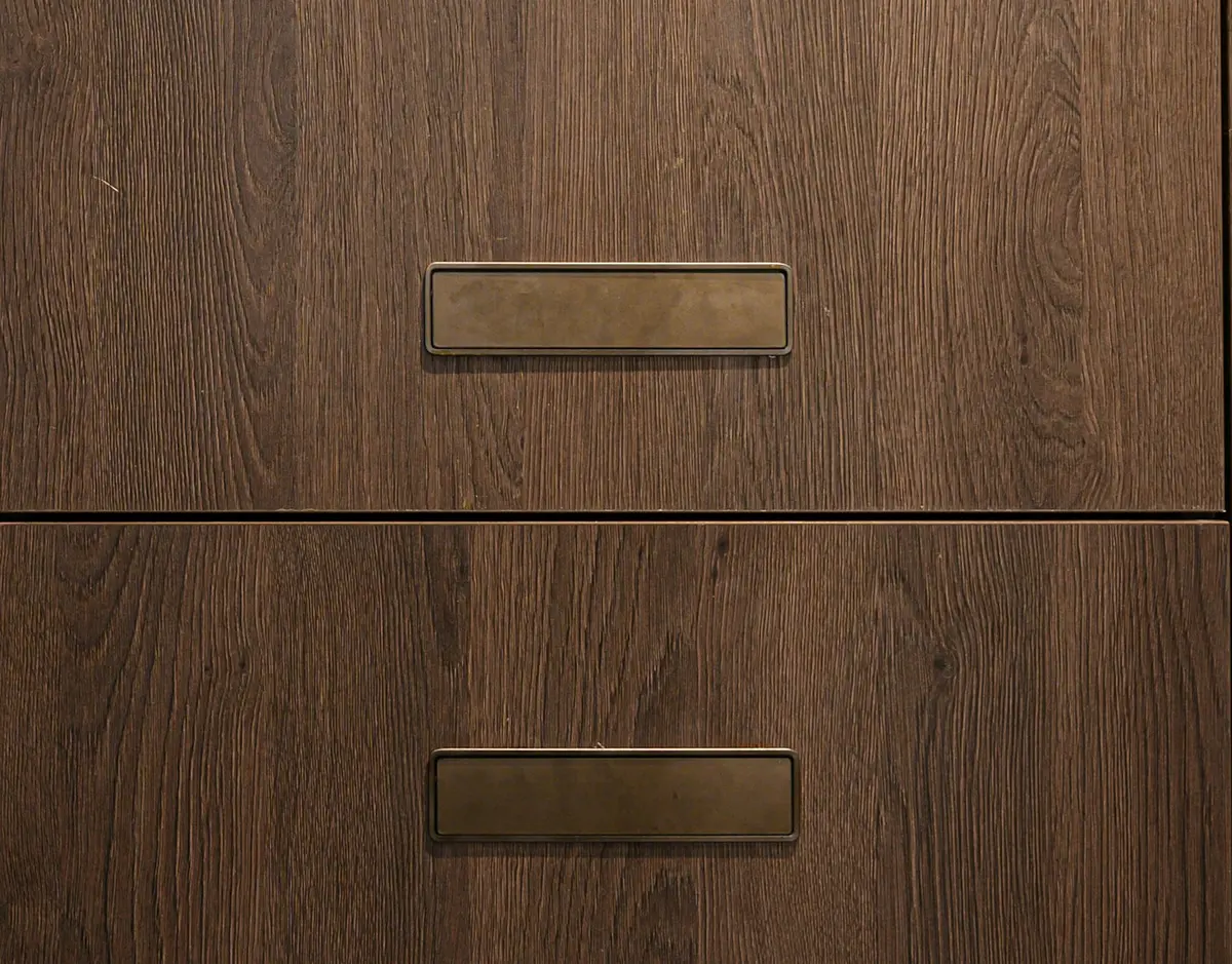 Close-up of dark oak wood-grain cabinet fronts with slim bronze pull handles