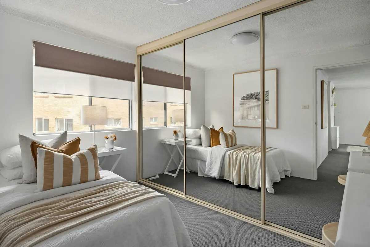 Bedroom with a wall-to-wall wardrobe of mirrored sliding doors in thin champagne frames reflecting the bed