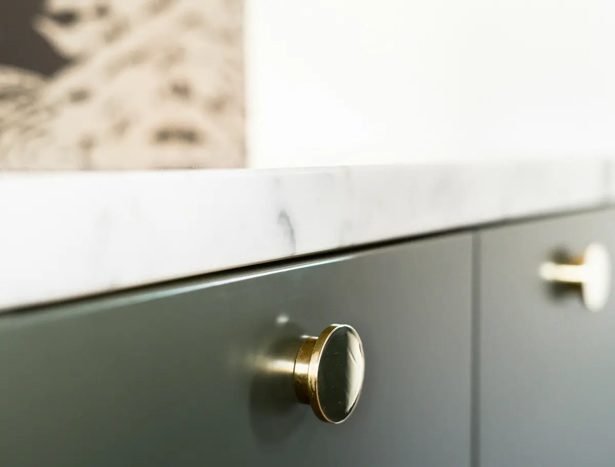 Close-up of matte dark green cabinet fronts with a brass knob under a white marble top