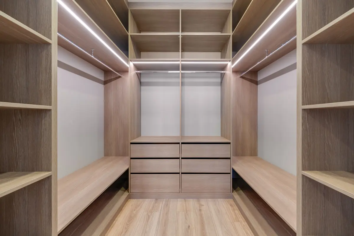 Oak-finish walk-in wardrobe with LED strip lights along the shelf edges and a drawer unit at the far end