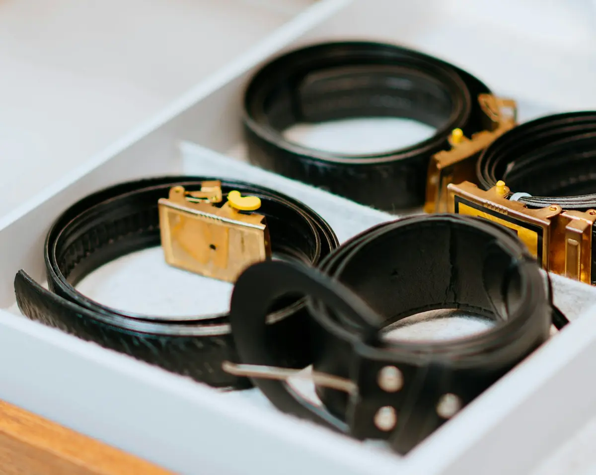 Leather belts coiled in a divided white organiser tray on a wooden pull-out