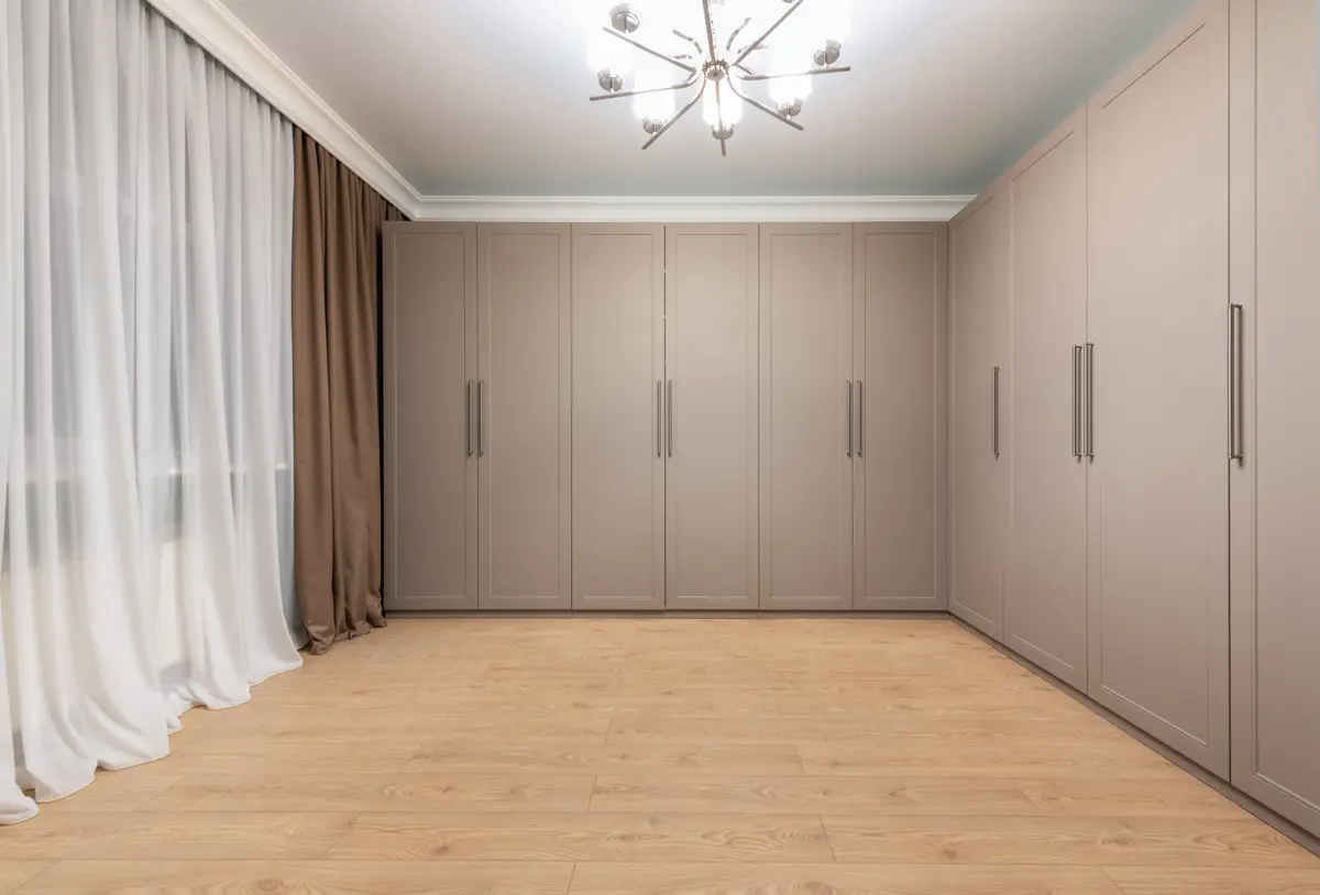 Taupe floor-to-ceiling wardrobe with panelled hinged doors running around the corner of an empty room