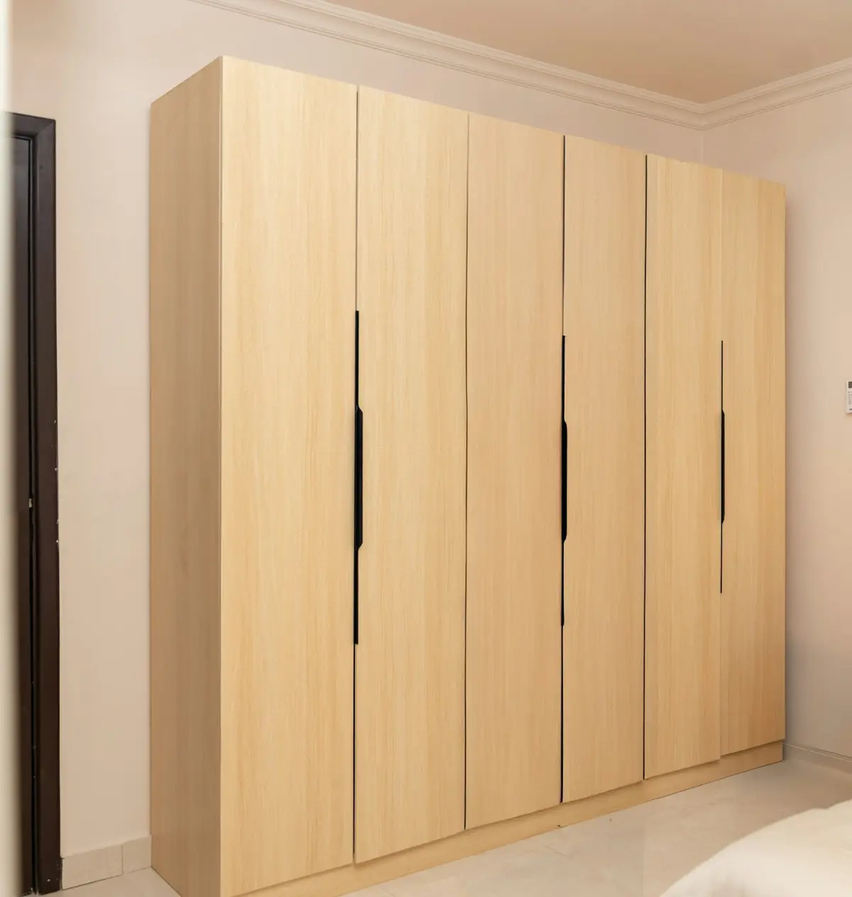 Light oak-finish wardrobe with hinged doors and slim black recessed pulls in a bedroom with a marble floor